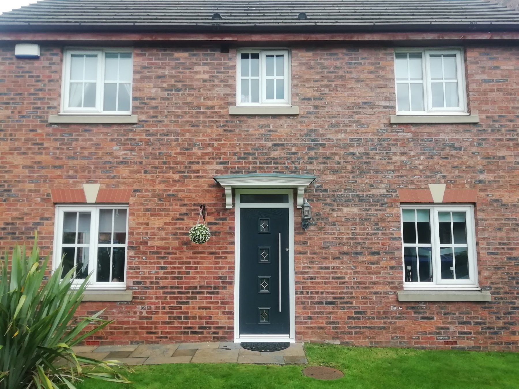A brick house with new white windows on both floors and a dark green front door