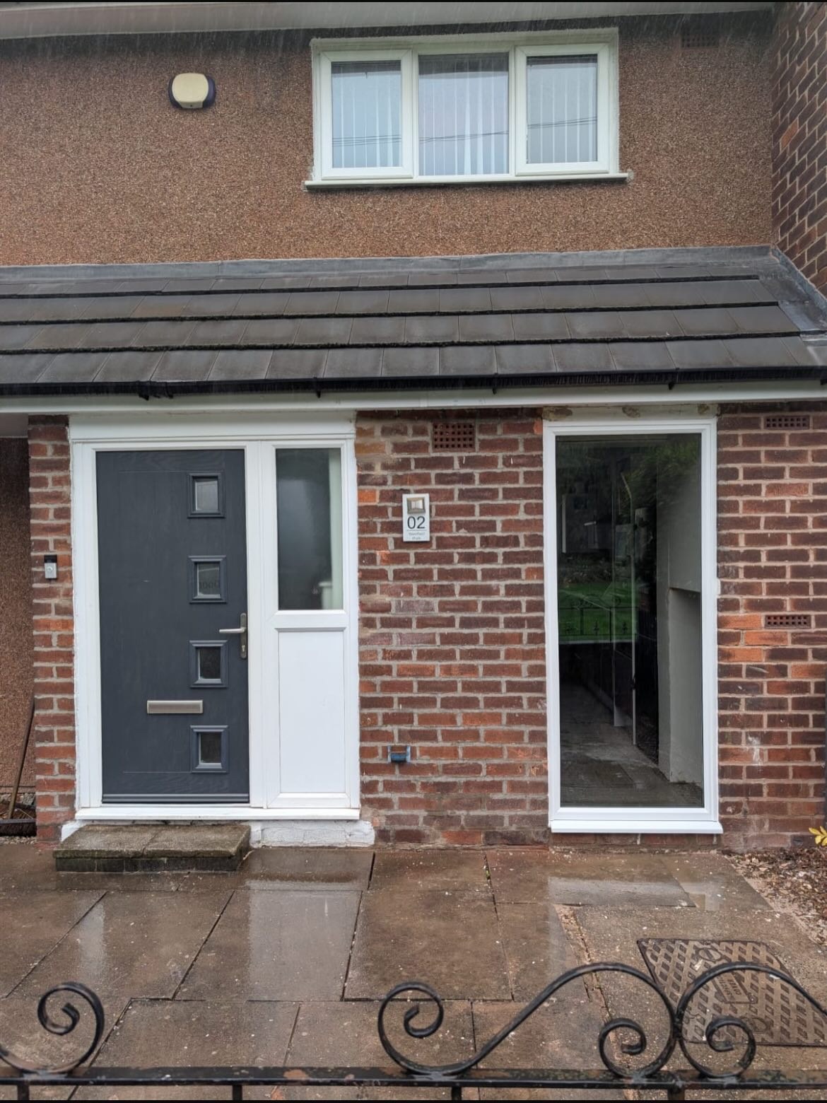 A grey composite door with a glazed side panel on a brick house