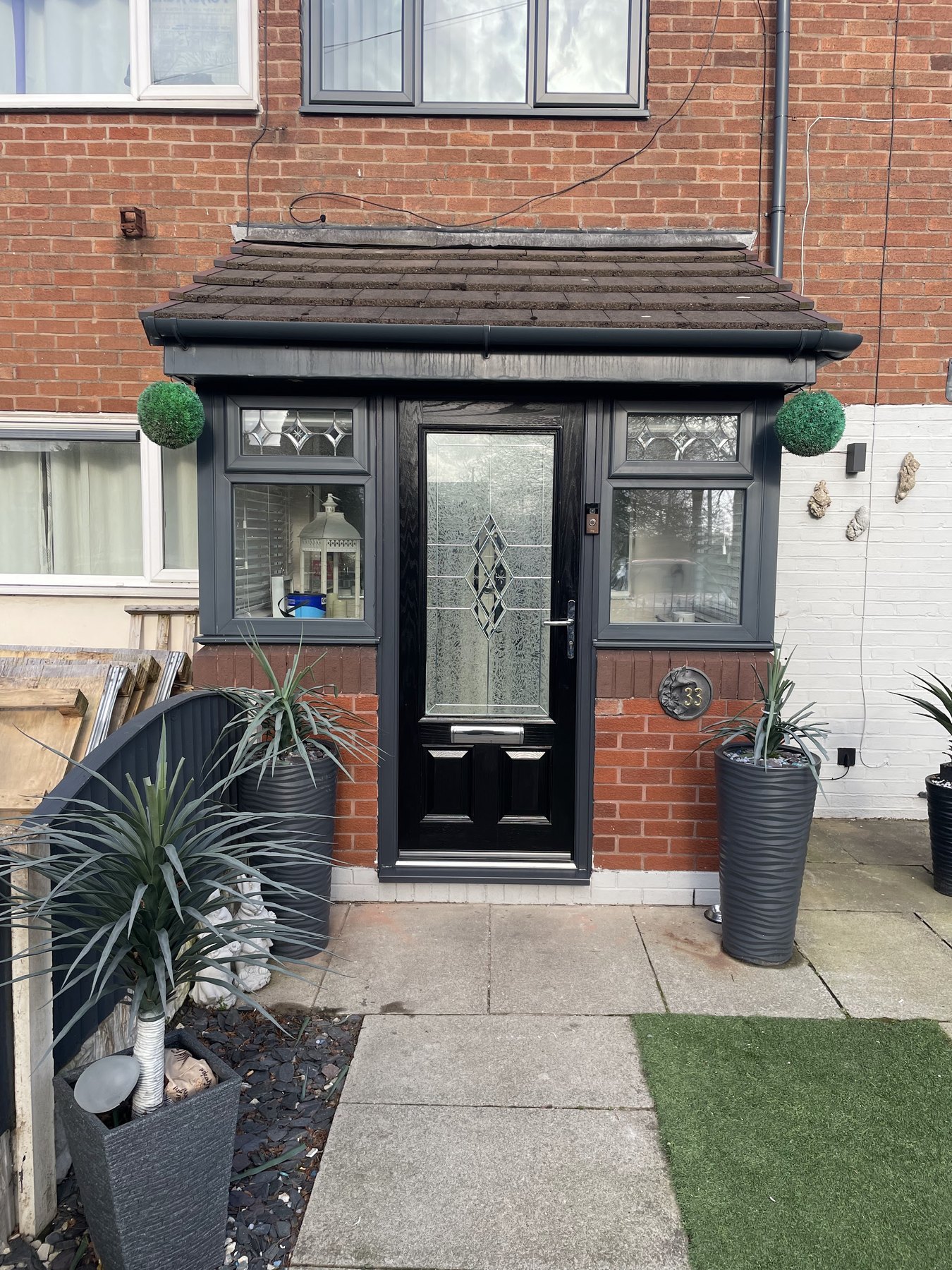 A porch with a black composite front door and grey windows on a brick house