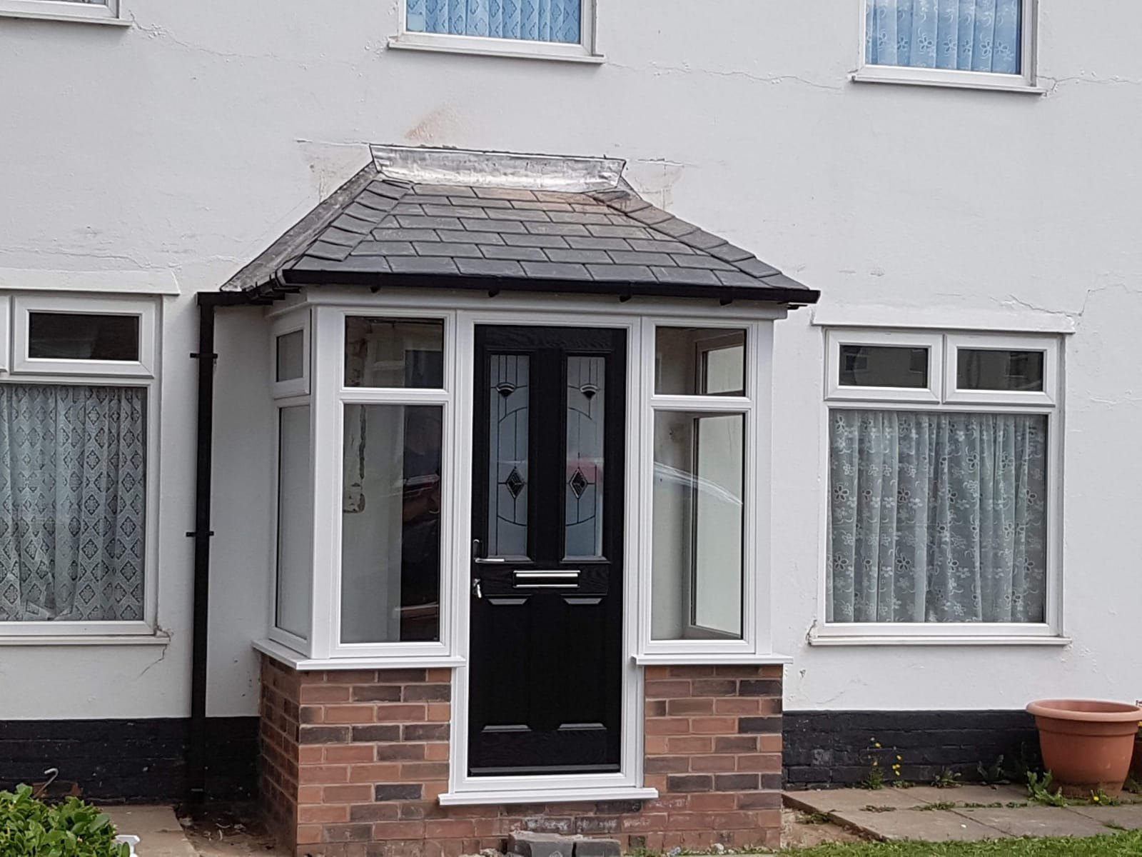 A new porch with a black composite door and white windows on a white rendered house